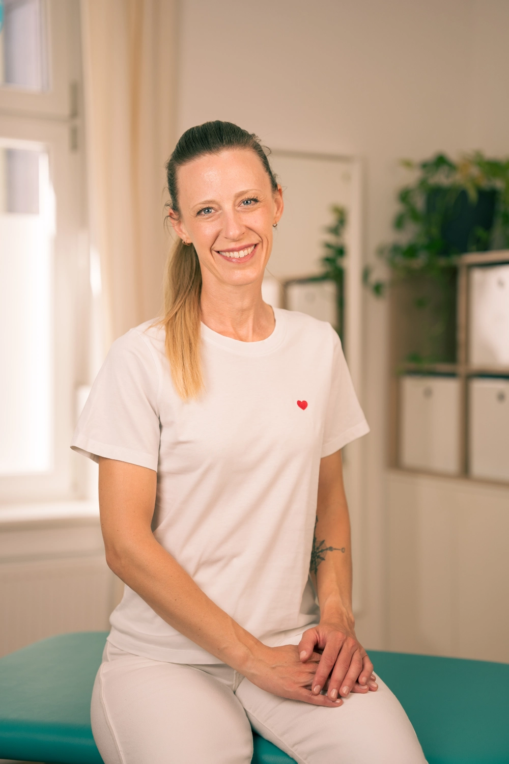 Kristina Wagner, Ergotherapeutin in Graz, sitzt lächelnd in ihrer Praxis auf einer Therapieliege